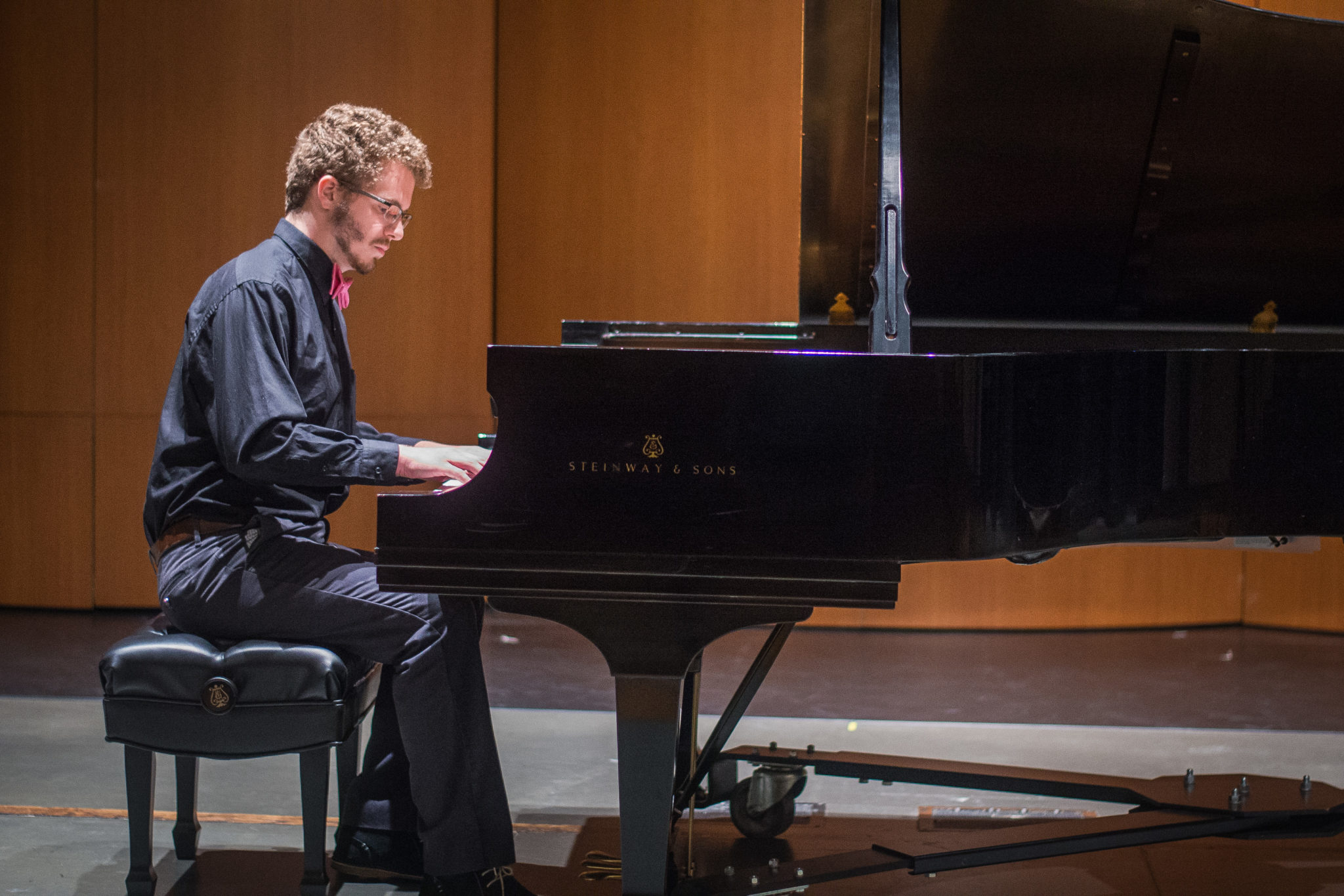 Student in black attire playing a grand piano on stage