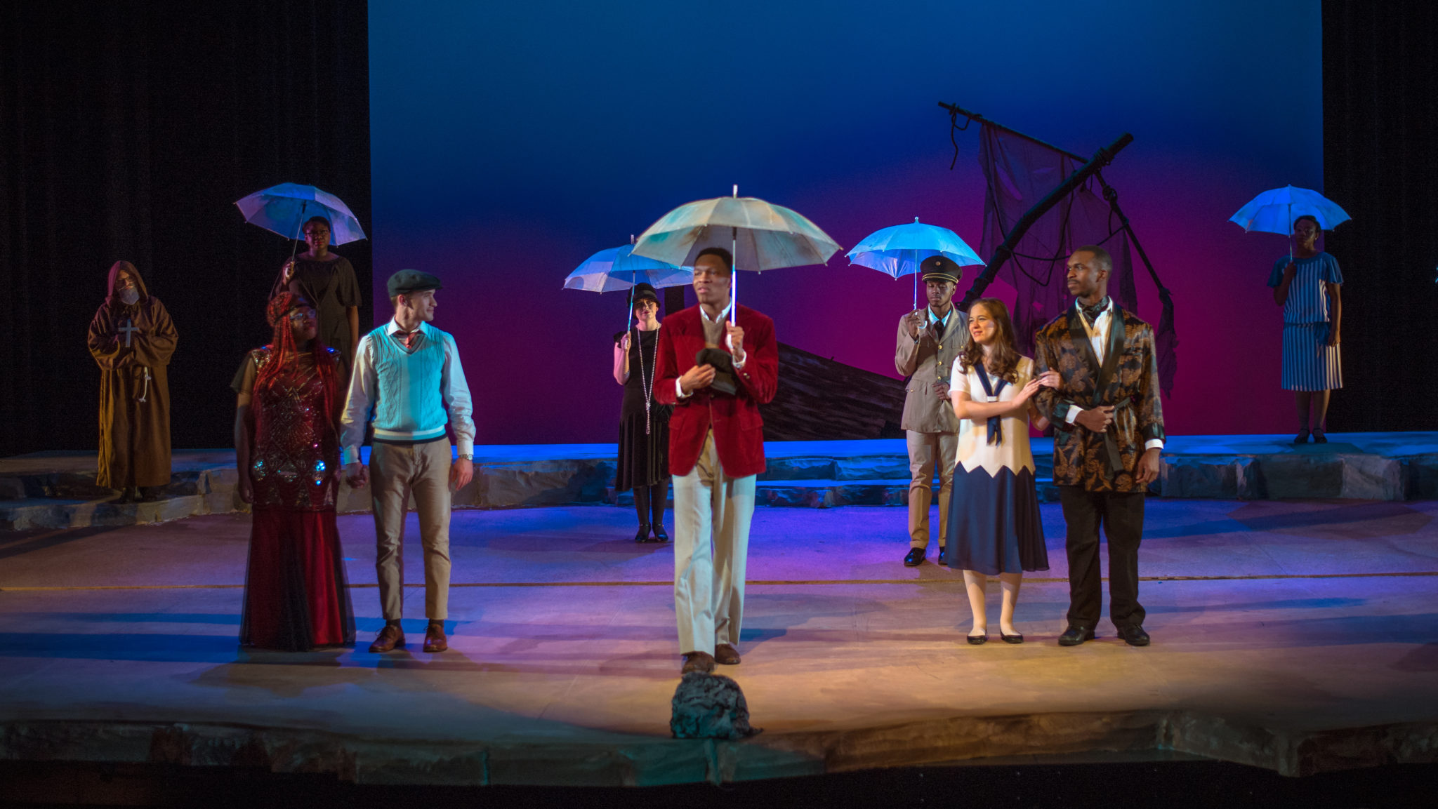Cast of Twelfth Night on stage, some holding umbrellas