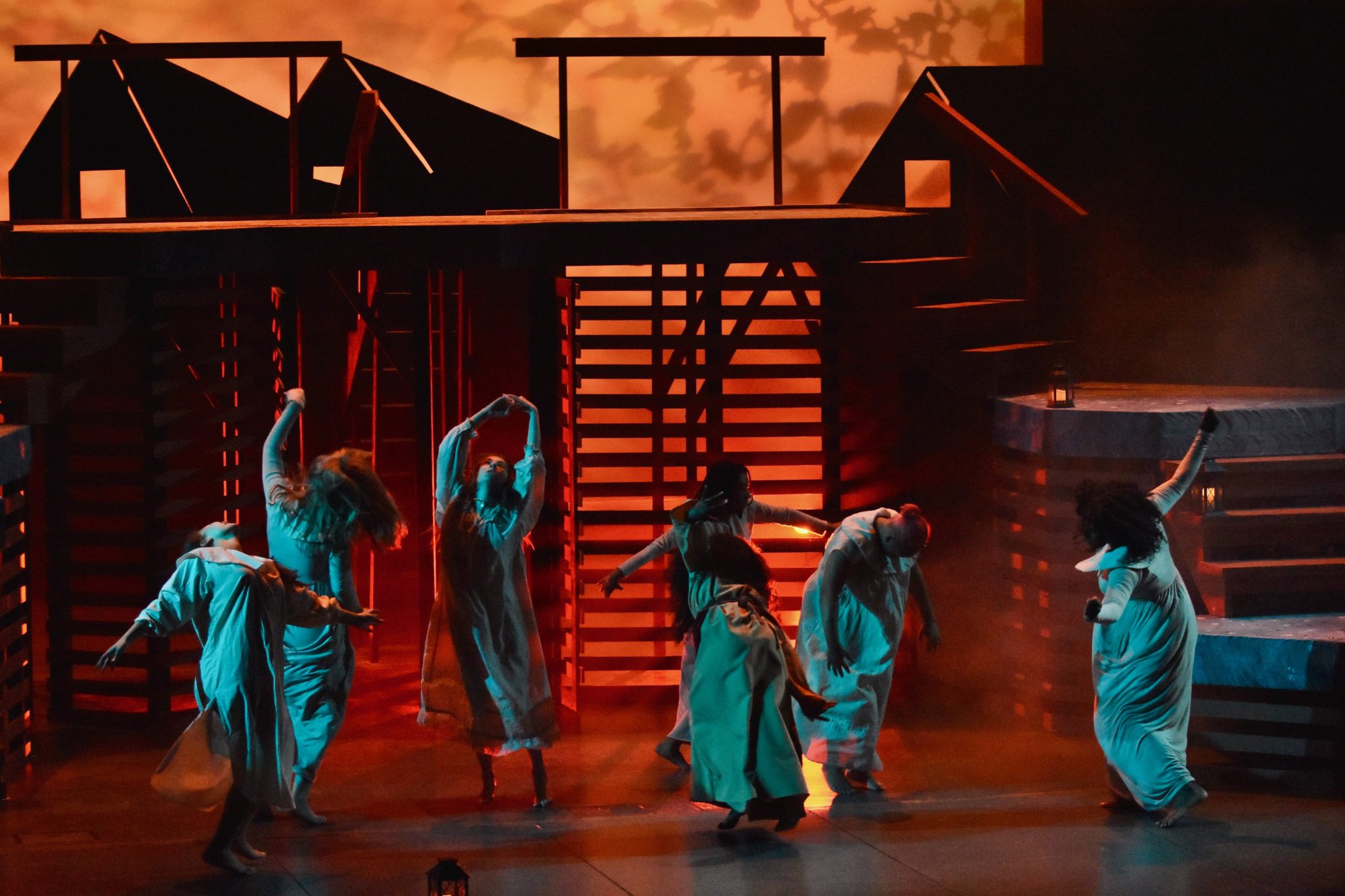 Students dancing on stage in white attire during a performance of the Crucible