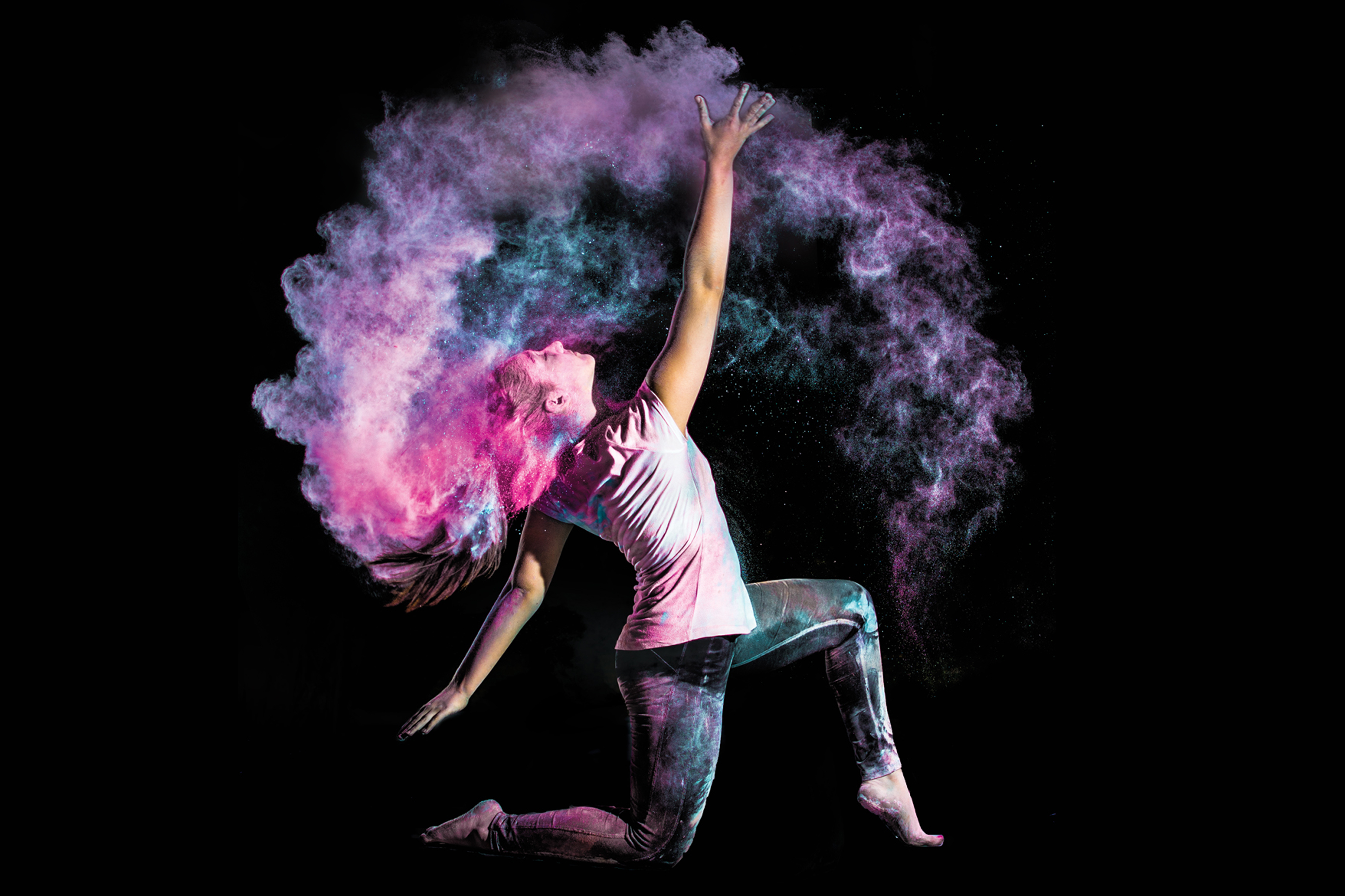 A dancer holds a pose on one knee while colorful powder spirals around her