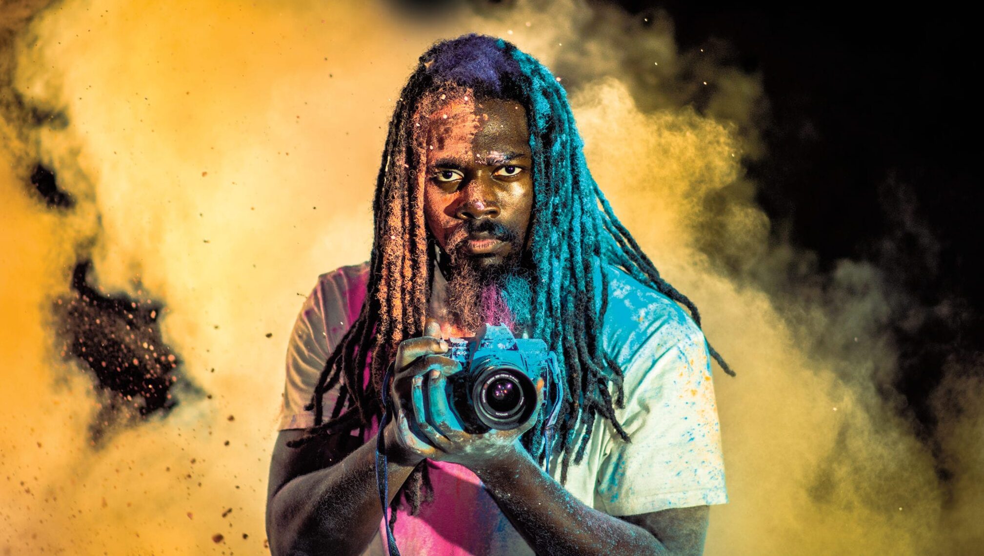 A photographer holds his camera in the midst of a cloud of colorful smoke or dust