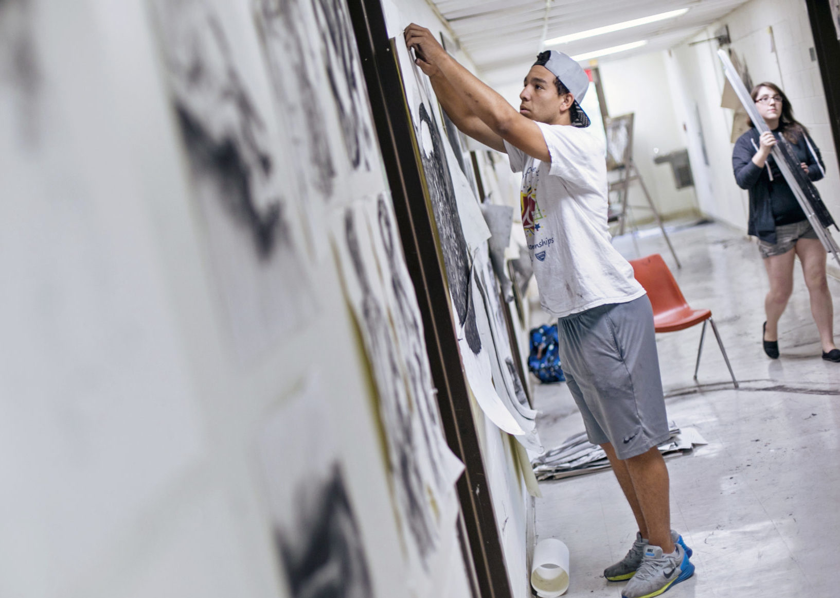 Student hanging art on the wall of a hallway