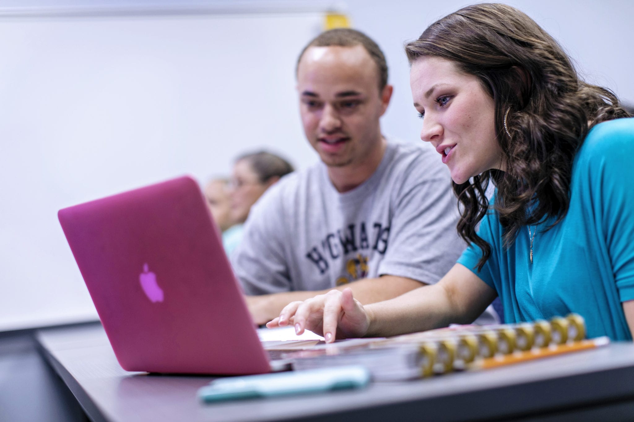 Two students look at a laptop while working in the classroom