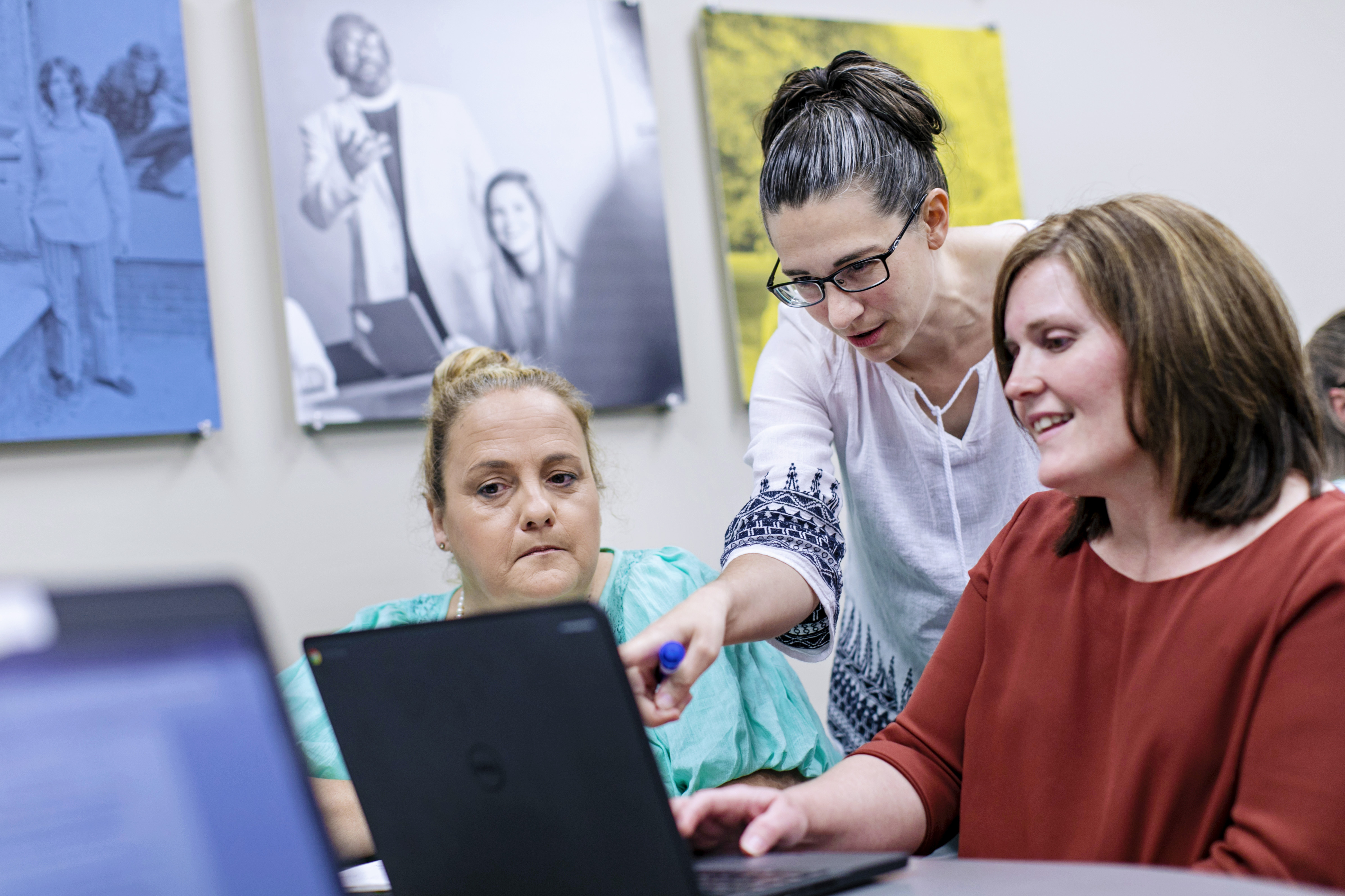 A professor points at a screen in the computer lab as two adult students look on