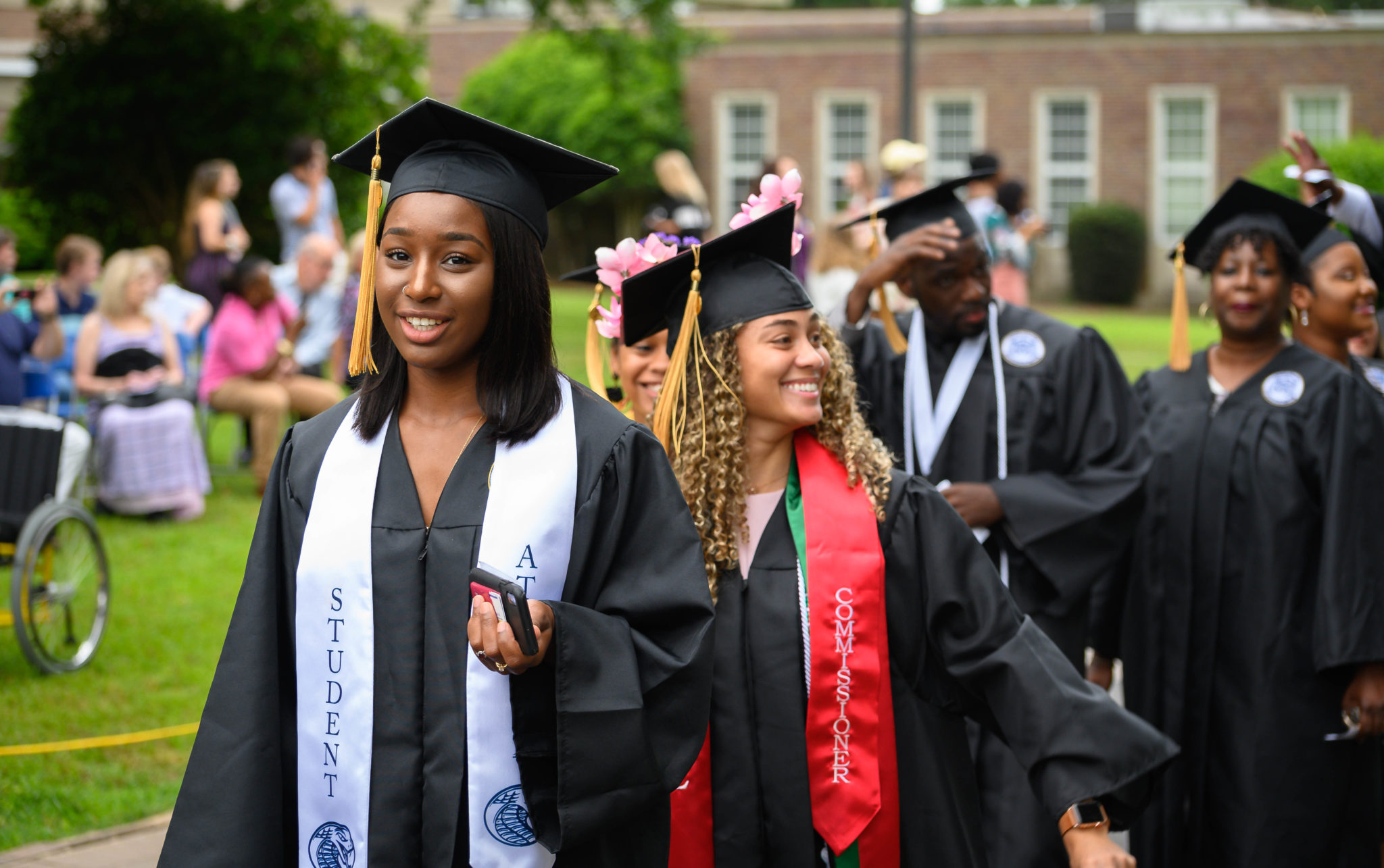 A student processes during an outdoor graduation ceremony, wearing a cap and gown