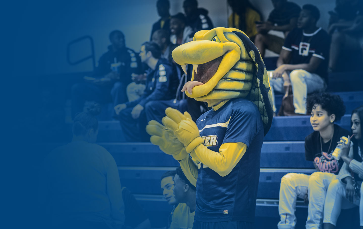 Striker the Cobra, the Coker Mascot, clapping in front of bleachers seated by students