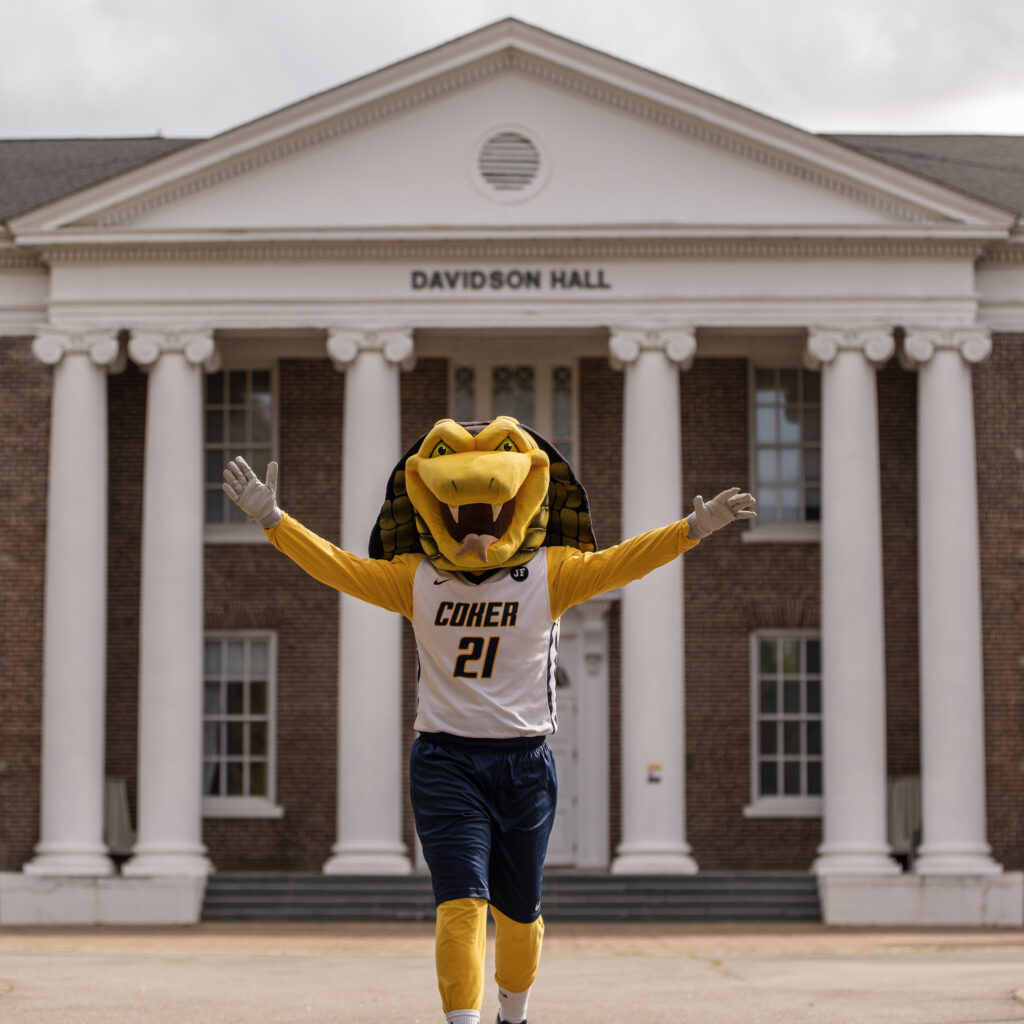 Coker Cobra's Mascot Striker the Cobra poses in front of Davidson Hall with his arms stretched out. 