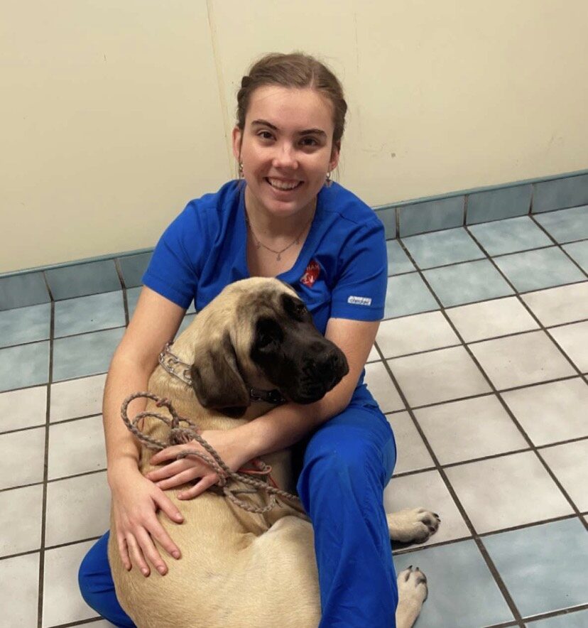 A student in scrubs poses with a dog on a tiled floor.